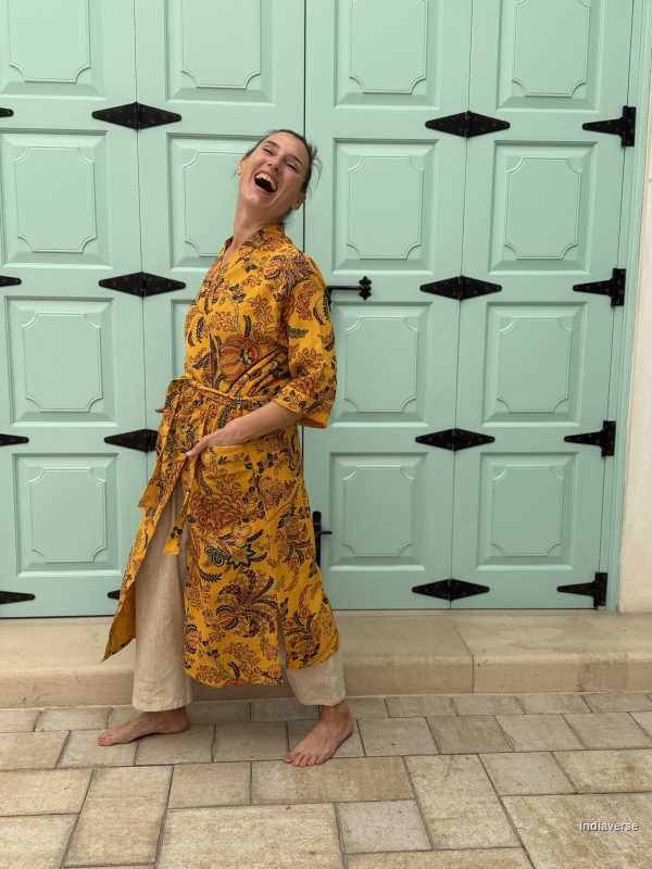 Woman wearing a yellow waffle cotton bathrobe with floral print, standing barefoot in front of a mint green door
