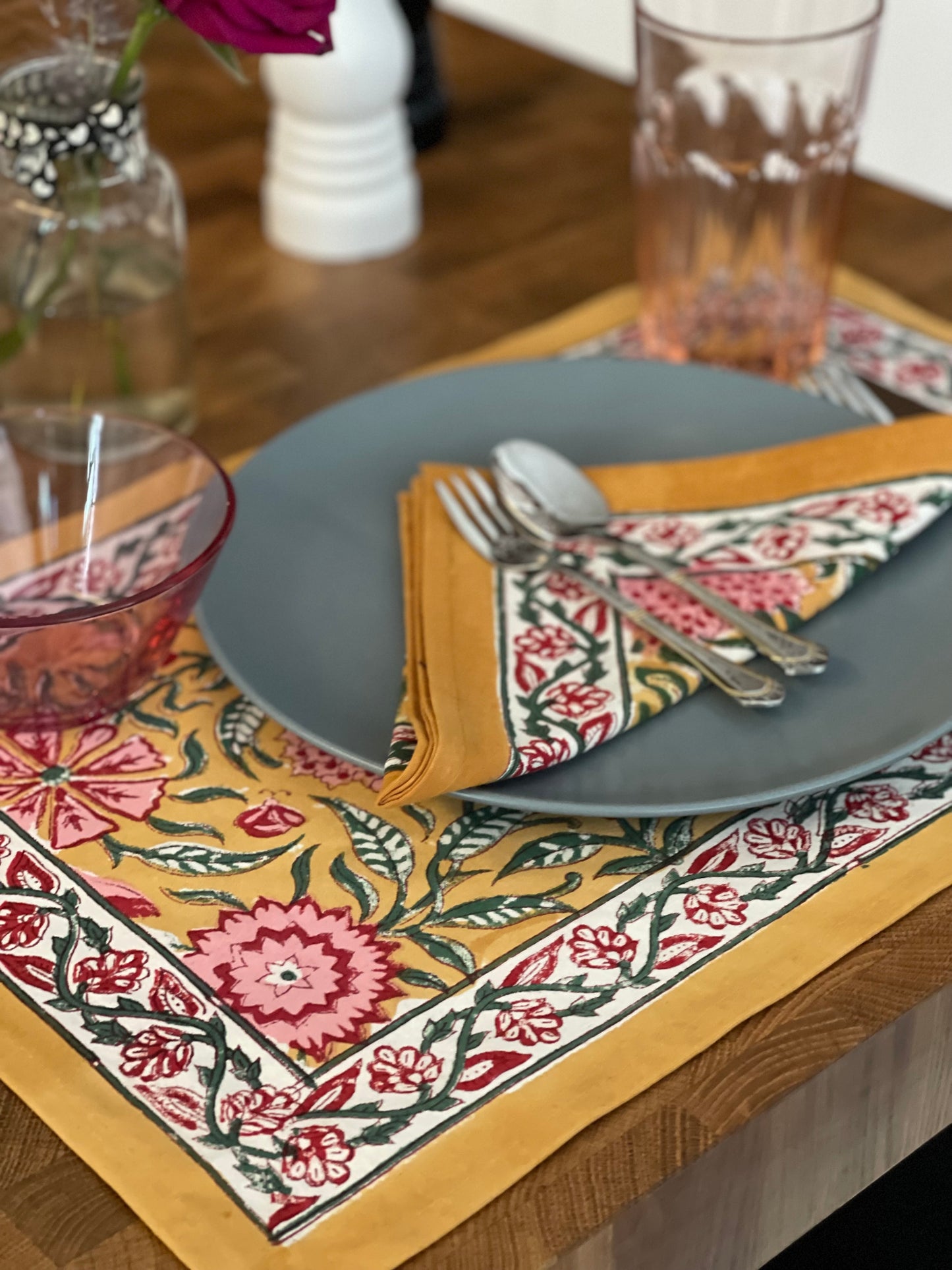 Decorative table setting with floral placemat, gray plate, and cutlery on a wooden table.