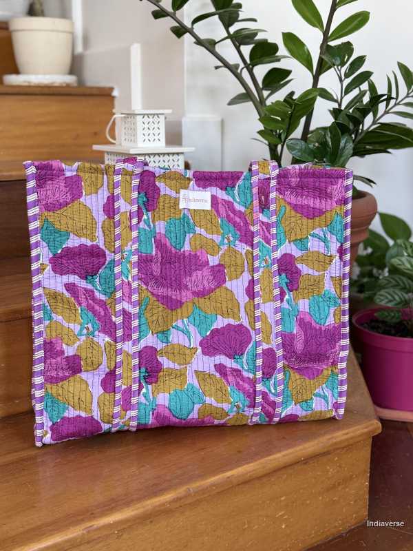 hand block printed quilted cotton tote bag with abstract purple flower design and perfect for shopping and carrying essentials sitting on wooden staircase with plants in the background
