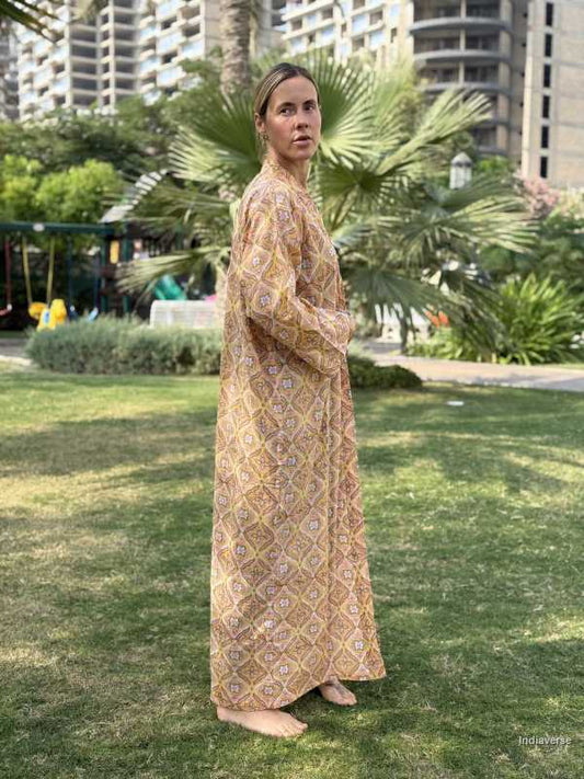 Woman in a patterned dress standing on grass with buildings and palm trees in the background