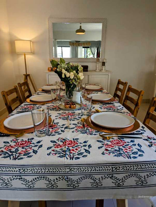 Dining table set with floral tablecloth, plates, and cutlery in a room with a mirror and lamp.