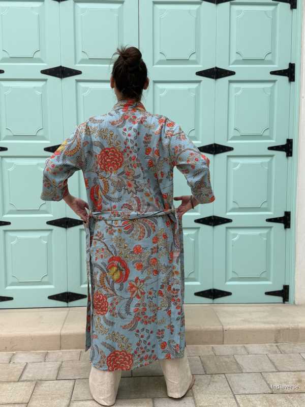 Back view of a woman wearing a blue waffle cotton bathrobe with vibrant floral print, posing in front of a pastel green paneled door