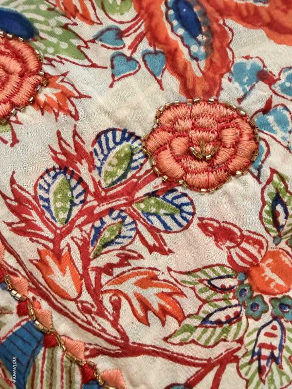 Close-up of embroidered fabric with floral patterns in red, blue, and green on a beige background.