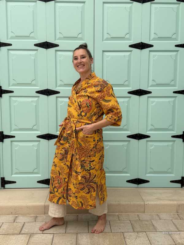 Woman wearing a yellow waffle cotton bathrobe with floral print, standing barefoot in front of a mint green door