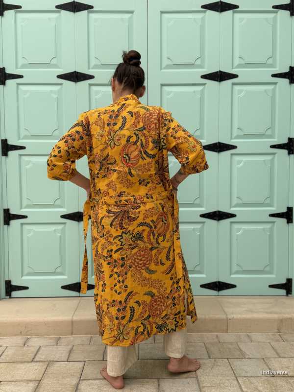 Woman wearing a yellow waffle cotton bathrobe with floral print, standing barefoot in front of a mint green door