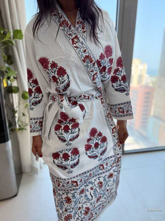 Person wearing a white dress with red floral patterns in a bright room.