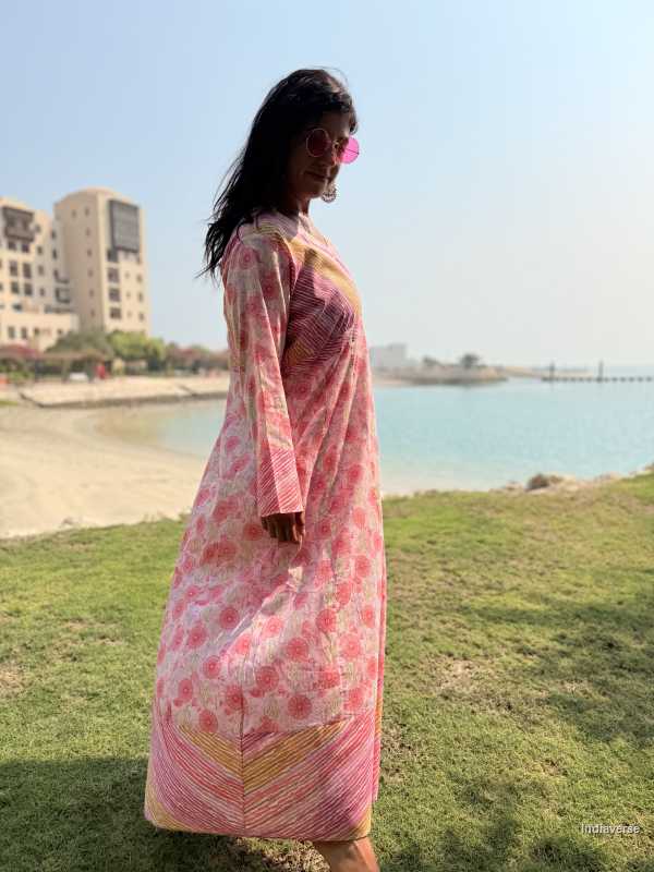 Woman in a pink dress standing on grass with a body of water and buildings in the background