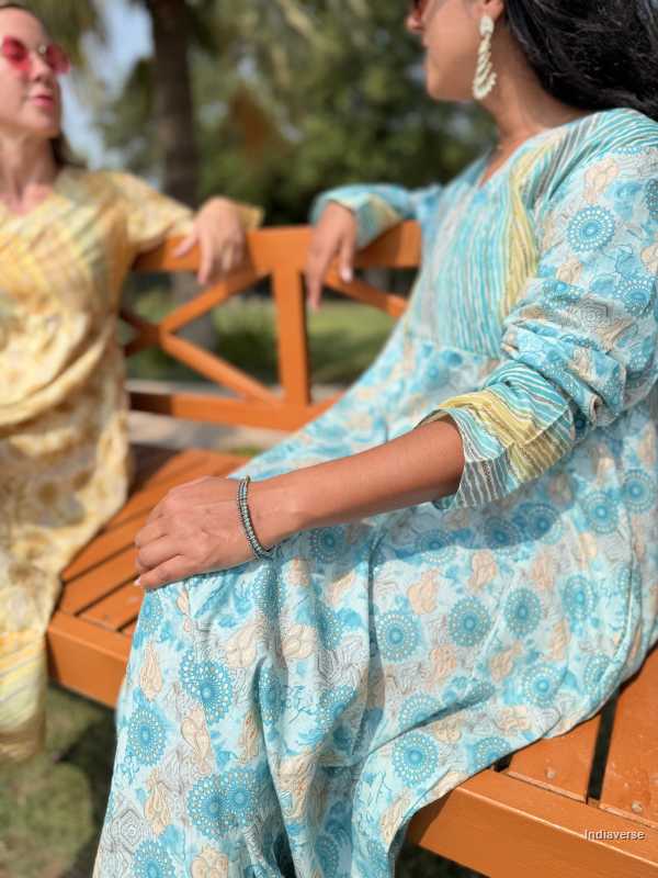 Woman in a blue patterned outfit sitting on a wooden bench outdoors.