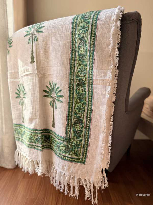 White blanket with green palm tree patterns draped over a chair.