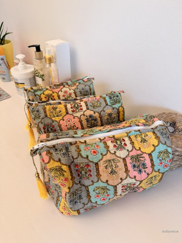 Three fabric cosmetic pouches with a colorful vintage floral and botanical pattern, arranged diagonally on a white surface with a tassel zipper pull | Arabesque