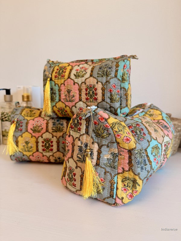 Three decorative cylindrical and rectangular storage pouches with a colorful patchwork floral pattern and yellow tassels, arranged on a white surface against a light beige background | Arabesque