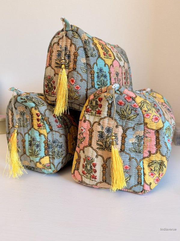 Three small quilted fabric pouches with yellow tassels, featuring a multicolor floral and botanical pattern in pastel shades of blue, pink, yellow, and green, arranged on a light surface against a plain light background | Arabesque
