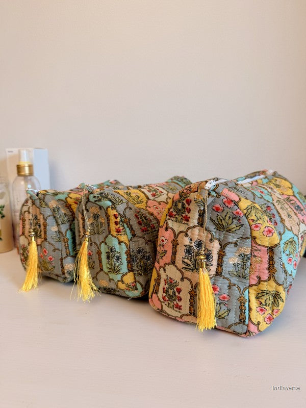 Three small zippered cosmetic pouches with yellow tassels, featuring a vintage floral and botanical pattern in muted tones of blue, green, pink, and yellow, arranged on a light surface against a plain beige background | Arabesque