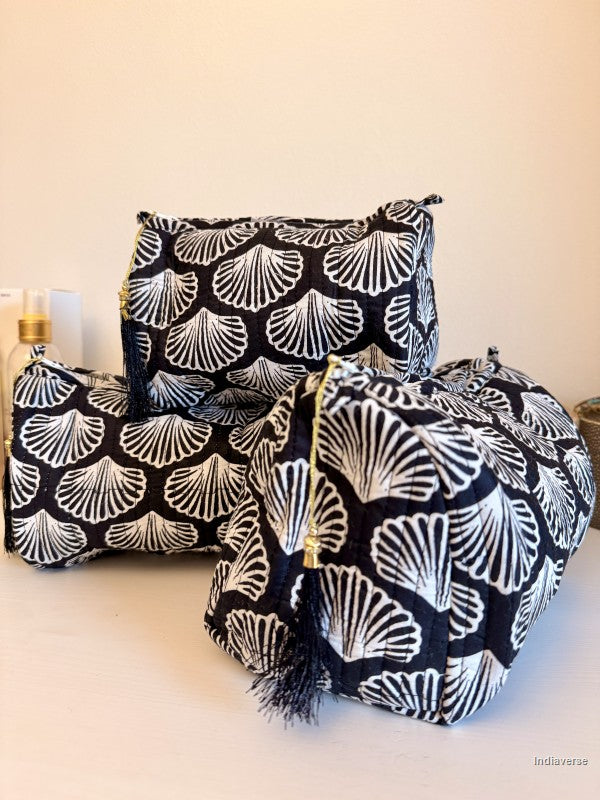 Three fabric cosmetic pouches with a black and white scallop pattern, featuring gold zippers and tassels, arranged on a light beige surface against a cream background | Black Sea Shell