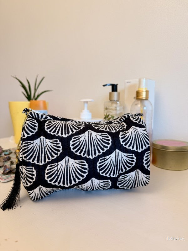A black and white patterned cosmetic pouch with a tassel zipper, displayed on a tabletop with decorative items in the background | Black Sea Shell