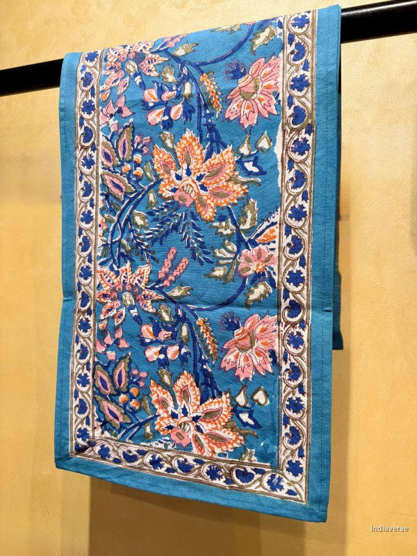 Blue and Floral design table runner hanging from a bar in front of a beige background