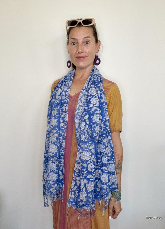 Woman wearing a blue scarf with white floral design standing in front of a white wall