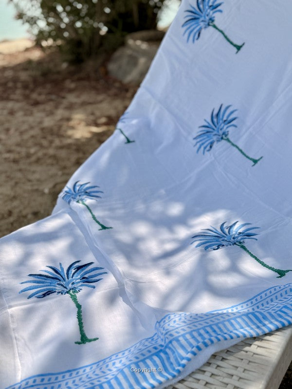 White towel with blue palm tree designs on a wicker chair outdoors.