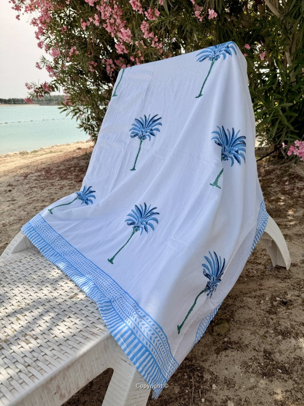 White towel with blue palm tree designs on a chair by a body of water.