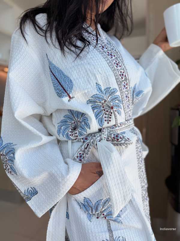 White embroidered robe with blue floral patterns worn by a person.