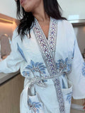 Woman wearing a white embroidered robe with blue patterns in a kitchen setting