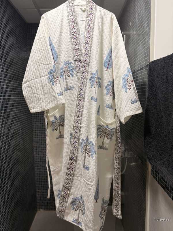 White robe with blue palm tree design hanging on a rack against a tiled wall.