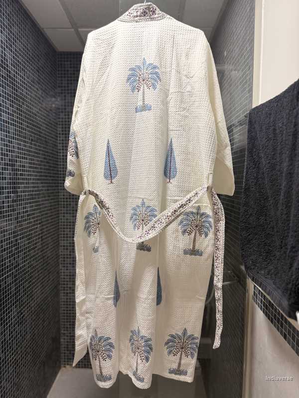 White embroidered robe with blue floral patterns hanging on a rack against a tiled wall.