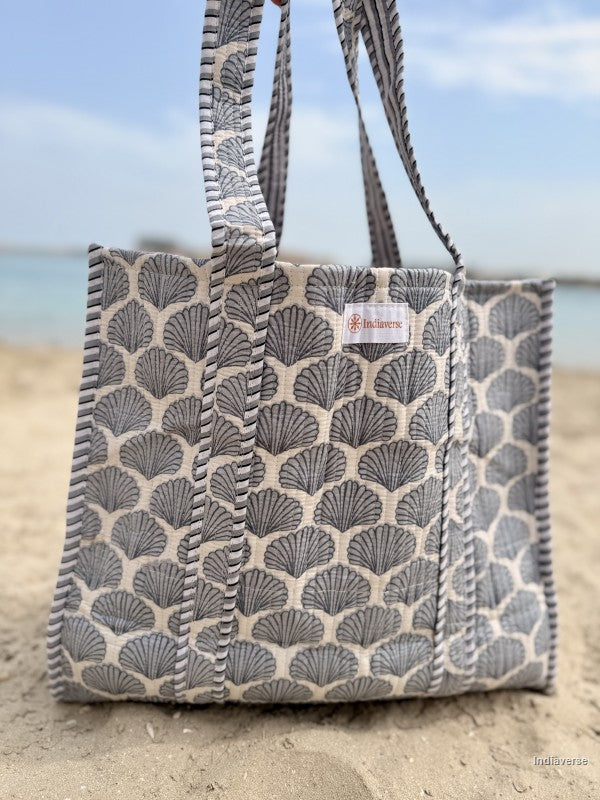 tote bag with blue sea shells design standing in the sand on a beach