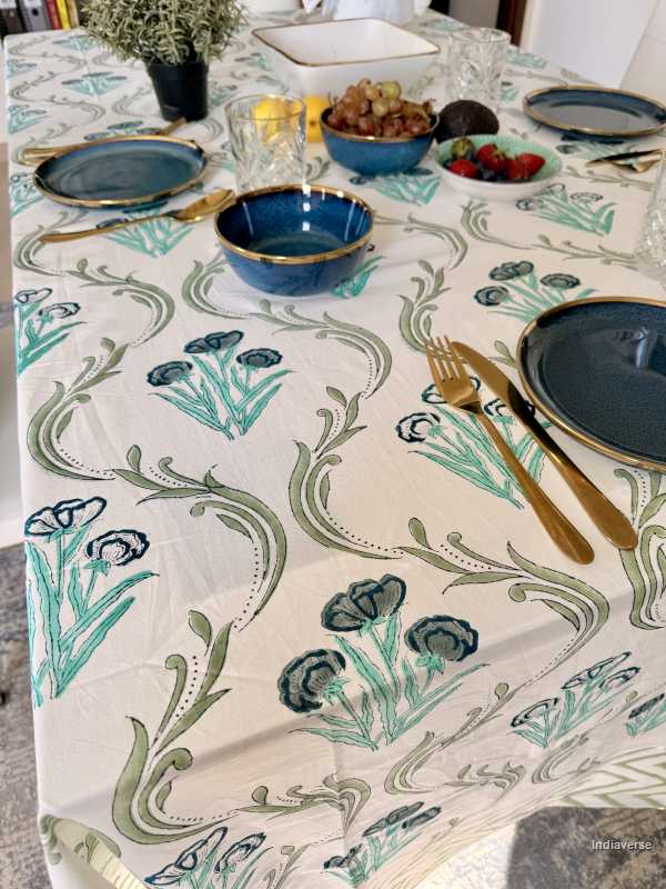 Dining table set with floral-patterned tablecloth, blue plates, and gold cutlery.