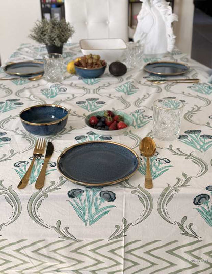 Dining table setting with floral-patterned tablecloth, plates, bowls, and cutlery.