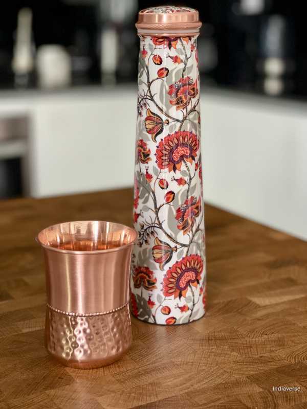 Tower shaped copper bottle with enameled red and grey floral design on a white base for carrying water with a capacity of 750 ml 