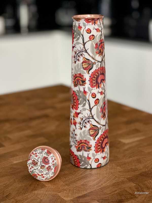 Tower shaped copper bottle with enameled red and grey floral design on a white base for carrying water with a capacity of 700 ml 