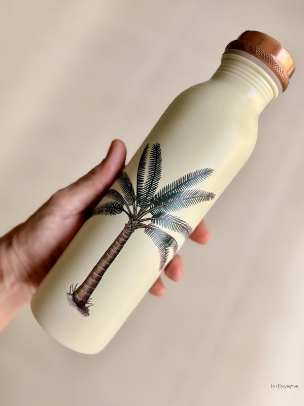 Someone holding a beige copper water bottle with single palm tree design in front of a neutral background