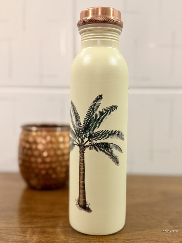 beige copper water bottle with single palm tree design standing on a brown surface with a copper cup in the background