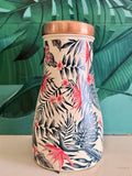 Copper water jar with tropical leaf and birds of paradise design sitting in front of a green leaf background