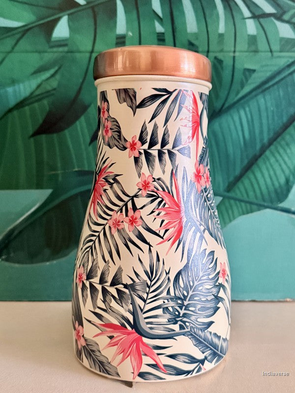 Copper water jar with tropical leaf and birds of paradise design sitting in front of a green leaf background
