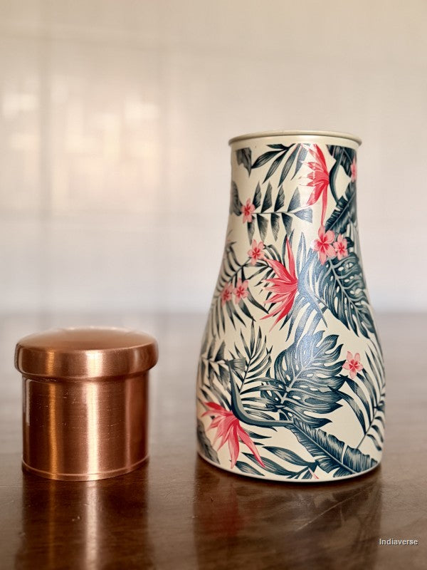 copper jar with tropical leaf and bird of paradise flower design sitting on a brown table with its lid