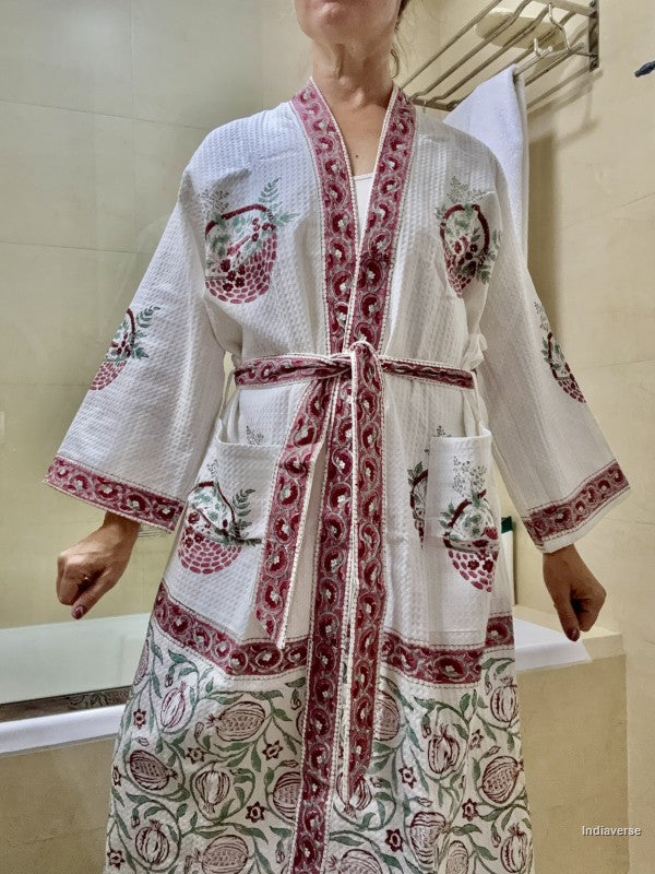 A woman wearing a white cotton bathrobe with red and green pomegranate and floral patterns, standing in a bathroom.