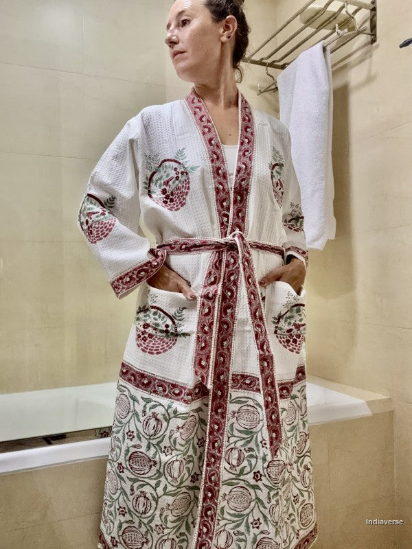 A woman wearing a white cotton bathrobe with intricate red and green floral embroidery, standing in a beige tiled bathroom.