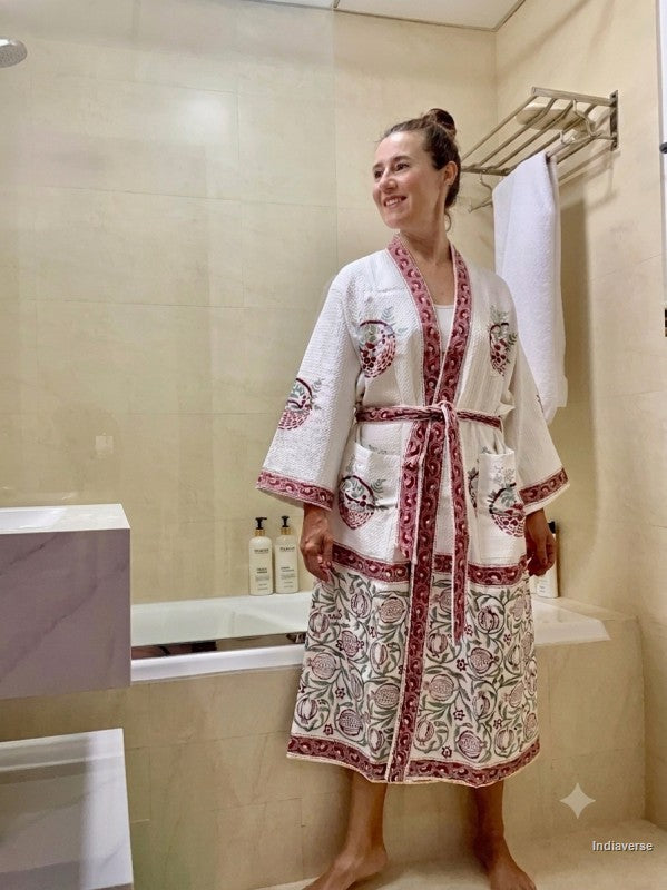 A woman wearing a white cotton bathrobe with red and green floral embroidery stands in a tiled bathroom next to a bathtub.