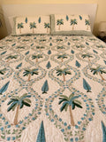 Cotton comforter on a queen size bed with blue and green palm tree design on a white background with two matching pillow cases