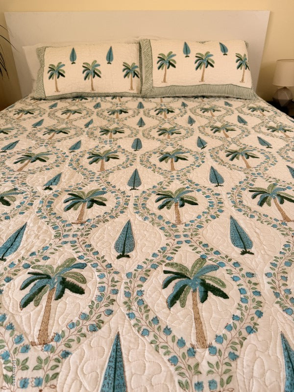 Cotton comforter on a queen size bed with blue and green palm tree design on a white background with two matching pillow cases