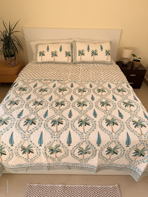 Cotton comforter on a queen size bed with blue and green palm tree design on a white background with two matching pillow cases