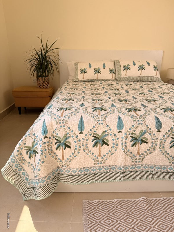 Cotton comforter on a queen size bed with blue and green palm tree design on a white background with two matching pillow cases