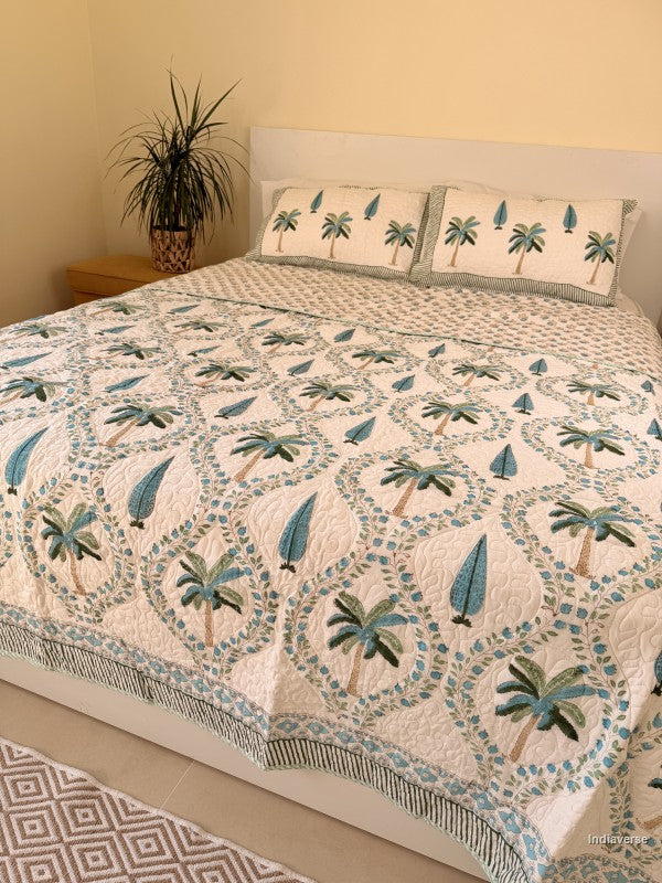 Cotton comforter on a queen size bed with blue and green palm tree design on a white background with two matching pillow cases