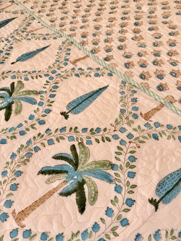 Cotton comforter on a queen size bed with blue and green palm tree design on a white background with two matching pillow cases