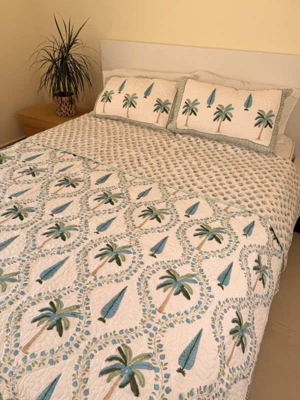 Cotton comforter on a queen size bed with blue and green palm tree design on a white background with two matching pillow cases