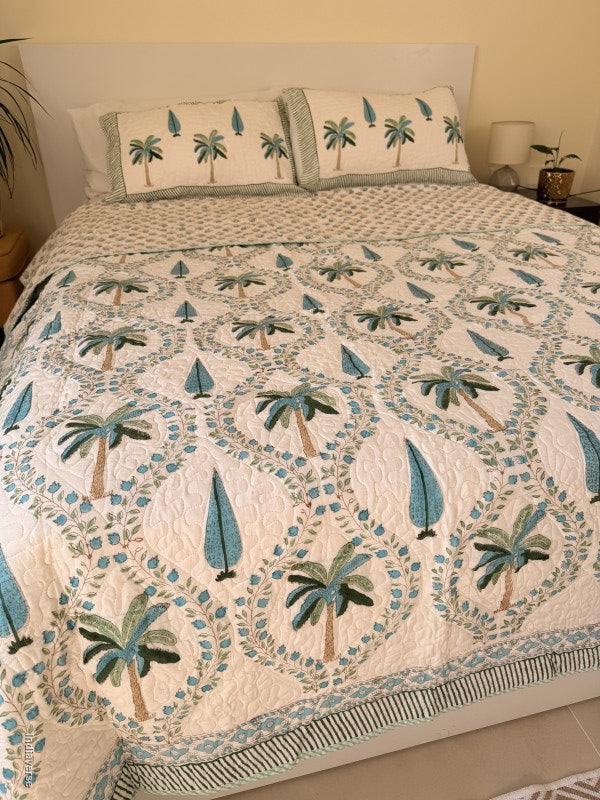 Cotton comforter on a queen size bed with blue and green palm tree design on a white background with two matching pillow cases