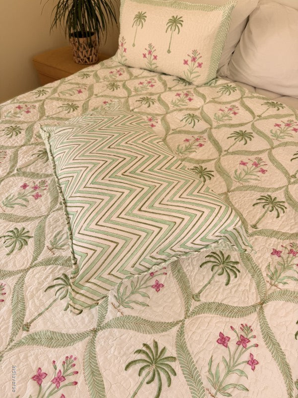 Cotton comforter with two matching pillow cases and floral and palm tree design arranged in arabesques on a queen size bed