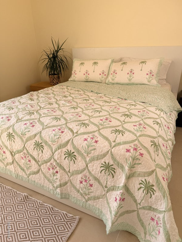 Cotton comforter with two matching pillow cases and floral and palm tree design arranged in arabesques on a queen size bed